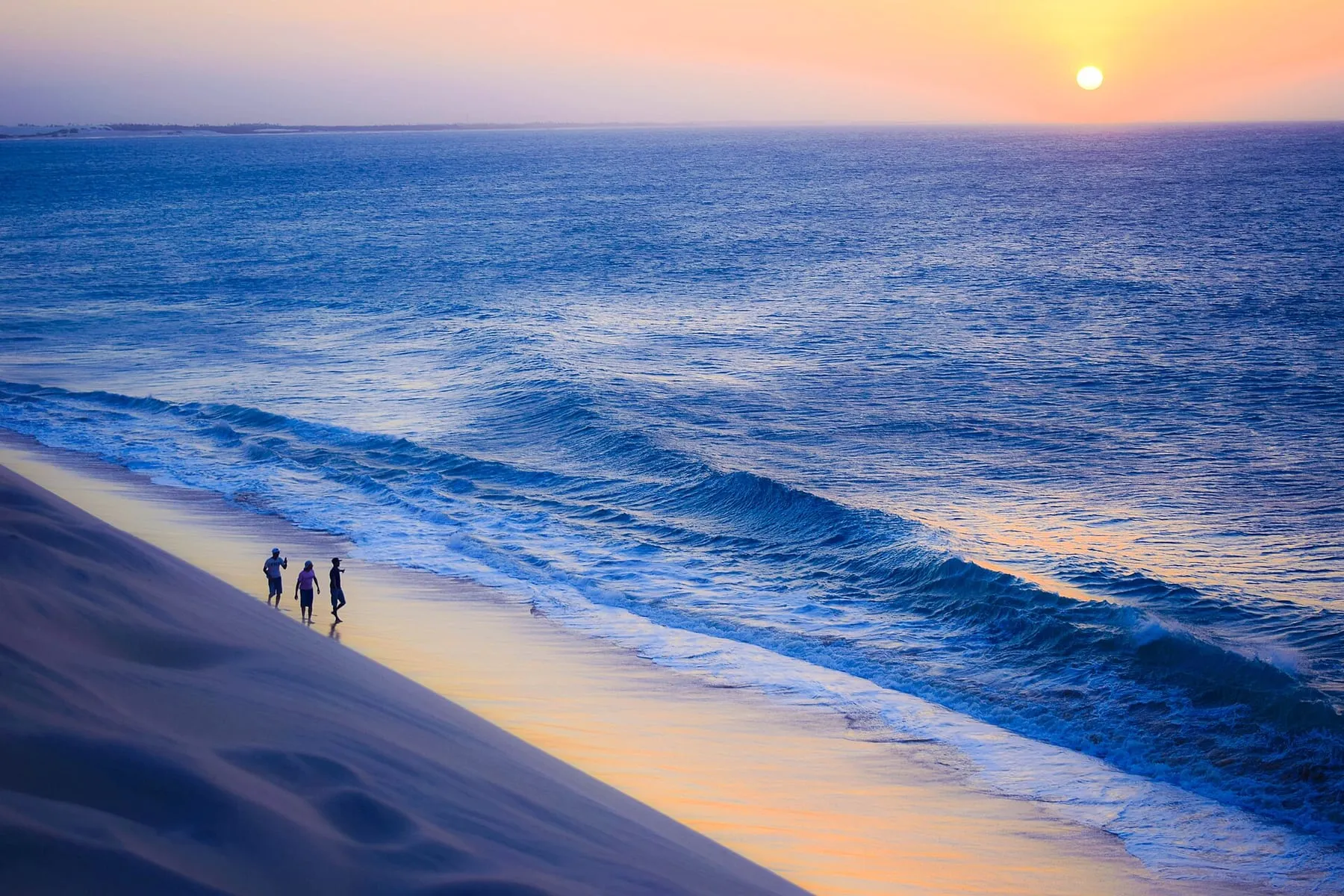 Pessoas caminhando no alto da Duna do Pôr do Sol com o mar de Jericoacoara ao fundo