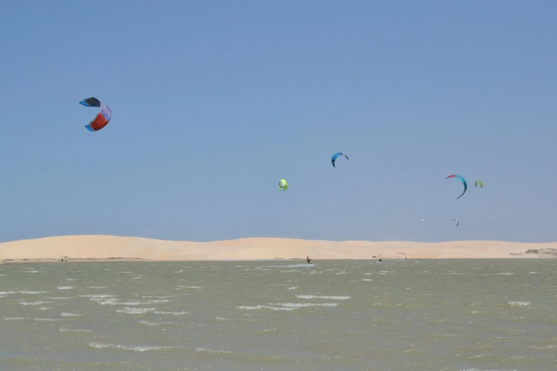 Várias pipas de kitesurf sobre uma lagoa rasa cercada de dunas