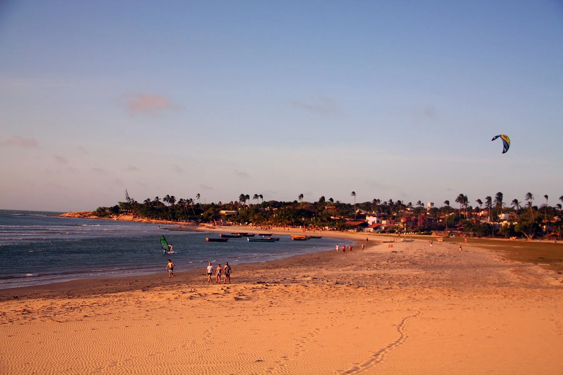 Vila de Jericoacoara vista da praia ao entardecer, com coqueiros e um kite no céu