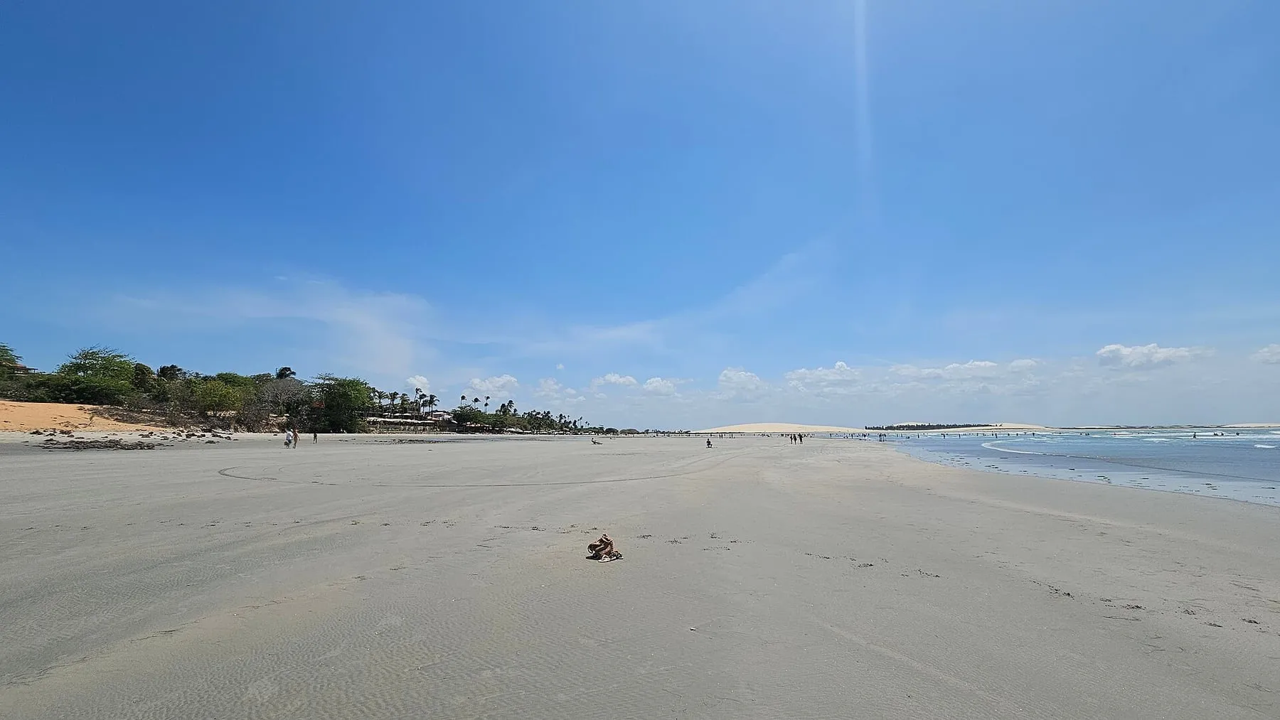 Faixa larga de areia da praia de Jericoacoara com dunas ao fundo